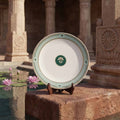 Decorative plate with a green emblem on a stand in front of stone architecture and water lilies.