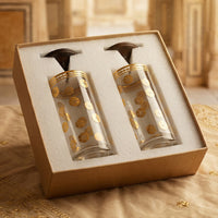 Two glasses with gold designs and wooden lid in a decorative box on a textured surface.