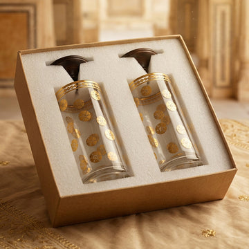 Two glasses with gold designs and wooden lid in a decorative box on a textured surface.
