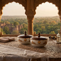 Two bowls with wooden lid, displayed on a stone ledge with a scenic outdoor view through arched stone windows in the background.