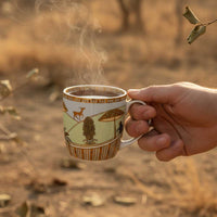 Hand holding a steaming mug with a scenic design in a natural setting