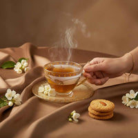 Steaming cup of tea with cookies and flowers on a brown fabric background