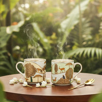 Two steaming mugs with nature-themed designs on a wooden table outdoors.