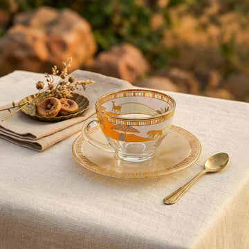Decorative glass teacup and saucer with gold patterns on a table with a blurred natural background