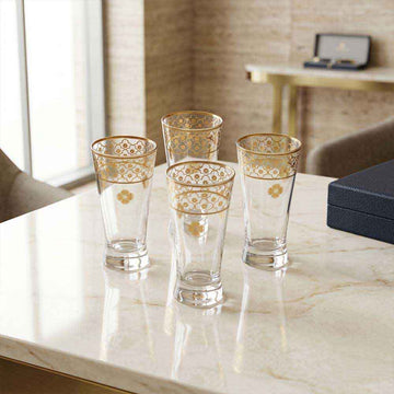 Set of four ornate glass tumblers on a marble surface with a blurred background