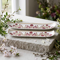 Two long rectangular ceramic serving trays with a floral pattern, displayed on a rustic stone block with cherry blossom branches.