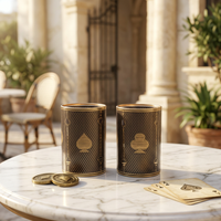 Two dark brown and gold playing card themed glasses with spade designs, displayed on a marble table with playing cards and coin lids in a luxurious outdoor patio setting.