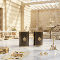 Two black and gold playing card themed glasses with spade symbols sit on a marble table in a sunlit stone patio setting, styled with a gold bell, playing cards, and jewelry.