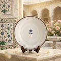 Decorative ceramic plate with floral design on a stand in an ornate interior setting.