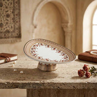 Decorative cake stand with floral patterns on a stone surface, with books and pearls in the background.