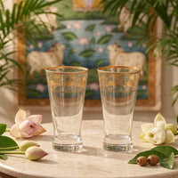 Two ornate glasses on a marble surface with flowers and a painting in the background