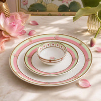 Set of ceramic plates and bowl with floral design on a marble surface with pink flowers and petals.
