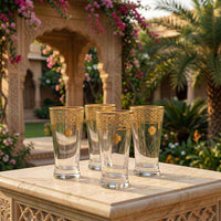 Set of four gold-trimmed glasses on a stone table with a garden and floral archway in the background.